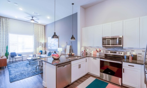 Model kitchen and living room at Cadence at Frisco Station Apartments in Frisco, Texas, featuring wood grain floor paneling.